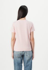 Camiseta de algodón de color rosa claro con mangas cortas y cuello redondo, combinada con jeans de denim azul desgastados, mostrando un diseño simple y casual.