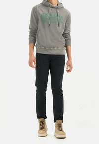 Gray hooded sweatshirt with green text, black pants, and beige sneakers. The sweatshirt features a kangaroo pocket and ribbed cuffs.