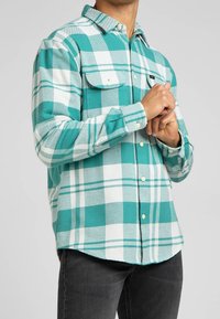 Chemise à carreaux turquoise et blanche en tissu doux, dotée d'une fermeture à boutons, de poches poitrine et de manches longues.