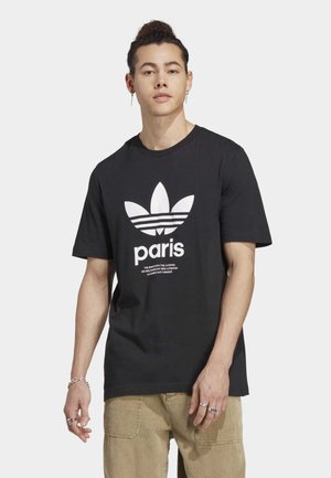 Black cotton t-shirt featuring a white Adidas logo with three stripes and the word "Paris" below. Short sleeves and a crew neckline.