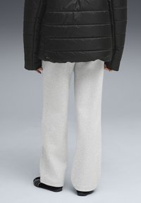 Svart puffjacka med horisontella sömmar, kombinerad med ljusgrå sweatpants. Byxorna är löst sittande och något strukturerade, med mörka strumpor.