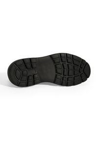 Schwarze Gummisohle mit einem strukturierten Grip-Muster, die dicke Profilrillen und einen glatten zentralen Bereich für Stabilität aufweist.