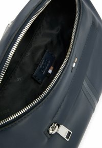 Interno di una borsa in pelle blu navy con una cerniera silver, etichetta con marchio e fodera nera. Presenta un design elegante e strisce orizzontali.