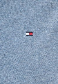 Jasnoniebieska bawełniana koszulka z krótkim rękawem z małym haftowanym logo w kolorach czerwonym, białym i granatowym. Materiał ma miękką, teksturowaną powierzchnię.