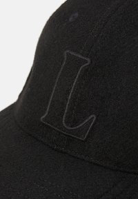Svart caps laget av filt med en strukturert overflate. Har et sydd "L"-logo i en litt mørkere nyanse av svart. Enkel design og struktur.