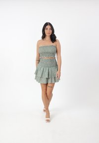 Grünes florales Zweiteiler-Set mit einem gesmokten Crop-Top und einem gestuften Mini-rock. Beinhaltet einen gewellten Rand und eine weiche Stofftextur.