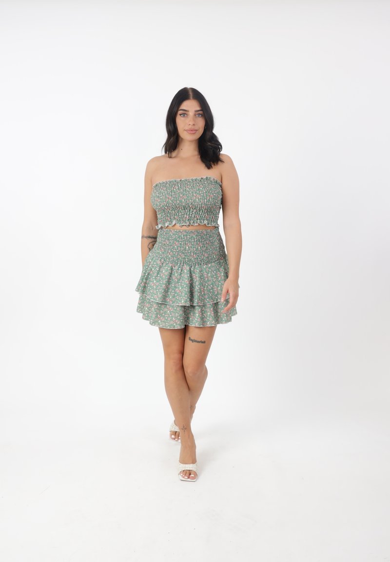 Grünes florales Zweiteiler-Set mit einem gesmokten Crop-Top und einem gestuften Mini-rock. Beinhaltet einen gewellten Rand und eine weiche Stofftextur.