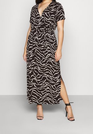 Frau trägt ein schwarz-weißes Wickelkleid mit Zebramuster, kurzen Ärmeln, seitlichem Schlitz und schwarzen, elegant geschnürten Sandalen mit hohen Absätzen.