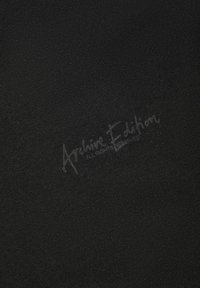 Zwarte stof met een gladde, licht gestructureerde oppervlakte. Bevat een vervaagd geprint logo met de tekst "Archive Edition" in een lichtgrijze tint.