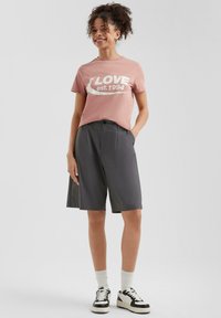 Lichtroze T-shirt met witte "LOVE est. 1994" grafiek, gecombineerd met donkergrijze shorts en zwart-witte sneakers met ribgebreide manchetten.