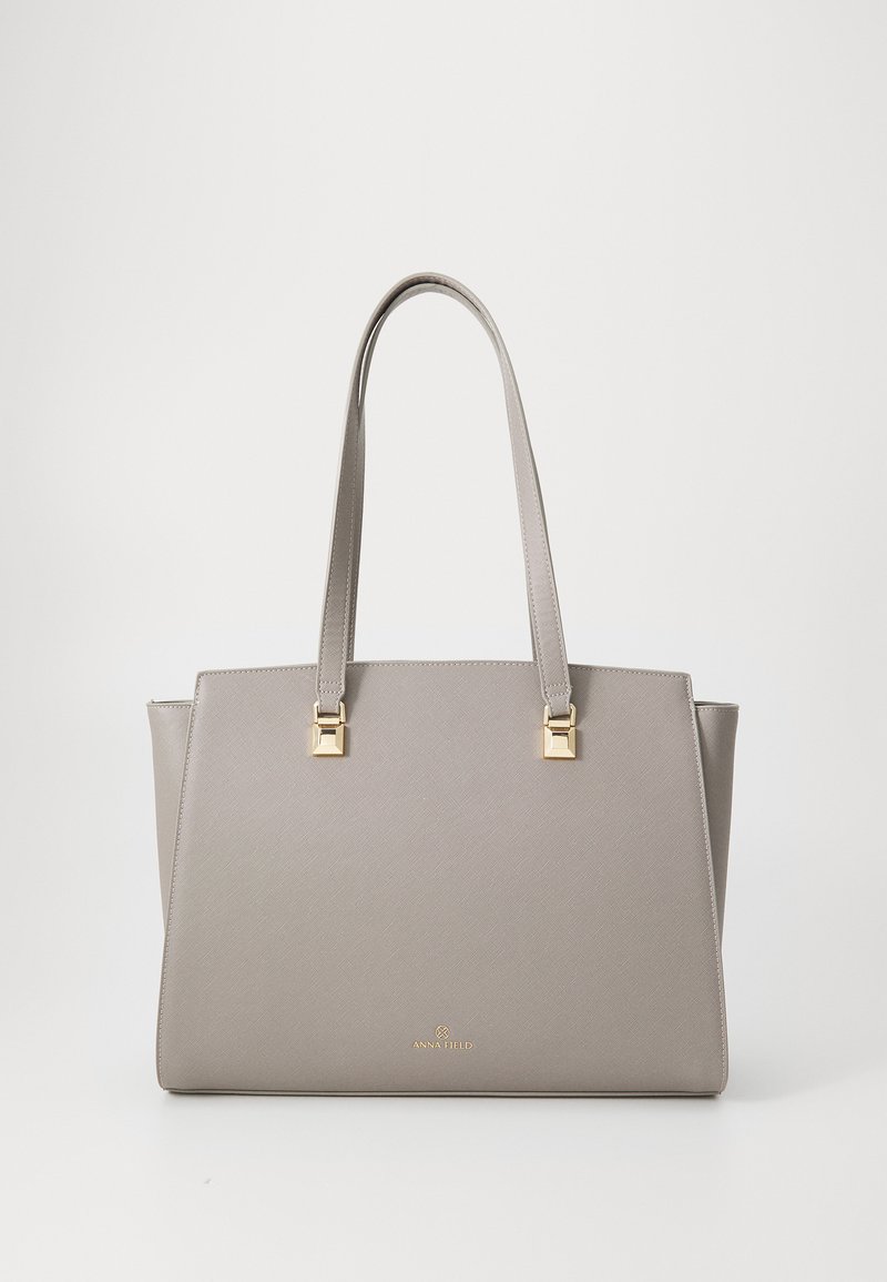 Graue synthetische Handtasche mit zwei langen Tragegriffen, goldenen quadratischen Hardware-Akzenten und einer strukturierten Oberfläche. Unten befindet sich ein goldenes Markenlogo.