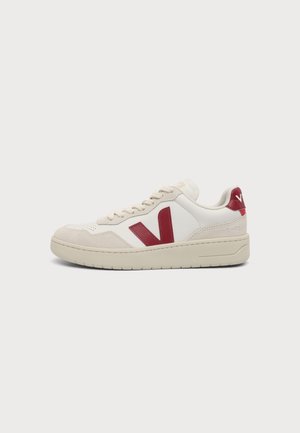 Άσπρο και μπεζ sneaker χαμηλής κοπής με κόκκινο λογότυπο "V" στο πλάι και κόκκινη ταμπέλα στη φτέρνα σε απλό φόντο.