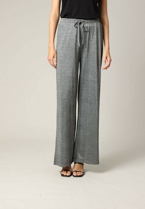Grijze wijde broeken met een glanzende afwerking, voorzien van een elastische tailleband en een verstelbaar trekkoord, gecombineerd met zwarte sandalen met bandjes.
