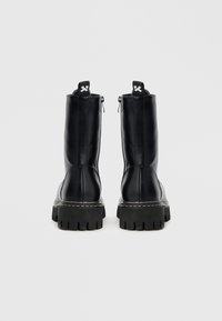 Botas de couro pretas até ao tornozelo, com acabamento texturizado, biqueira arredondada e sola grossa de borracha com rasto profundo; incluem fecho de correr traseiro e alças para facilitar o calçar.