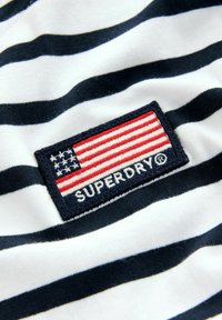 Bomull t-shirt med marinblå och vita horisontella ränder, med en vävd patch som visar den amerikanska flaggan och texten "SUPERDRY".