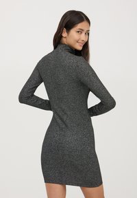 Czarna sukienka z prążkowanej tkaniny, dopasowana, z wysokim kołnierzem i długimi rękawami, o delikatnym, błyszczącym wykończeniu i krótkim dole.