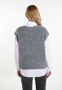 Grauer gestrickter Weste mit kurzen Ärmeln, mit geripptem Saum, getragen über einem weißen Hemd mit Knöpfen. Weiche Textur mit einer leicht lockeren Passform.