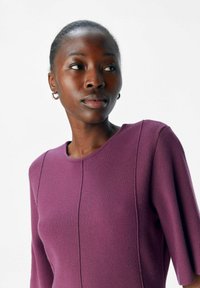 Lila stickad tröja med rund halsringning och mjuk textur. Har vertikala sömdetaljer och trekvartsärmar.