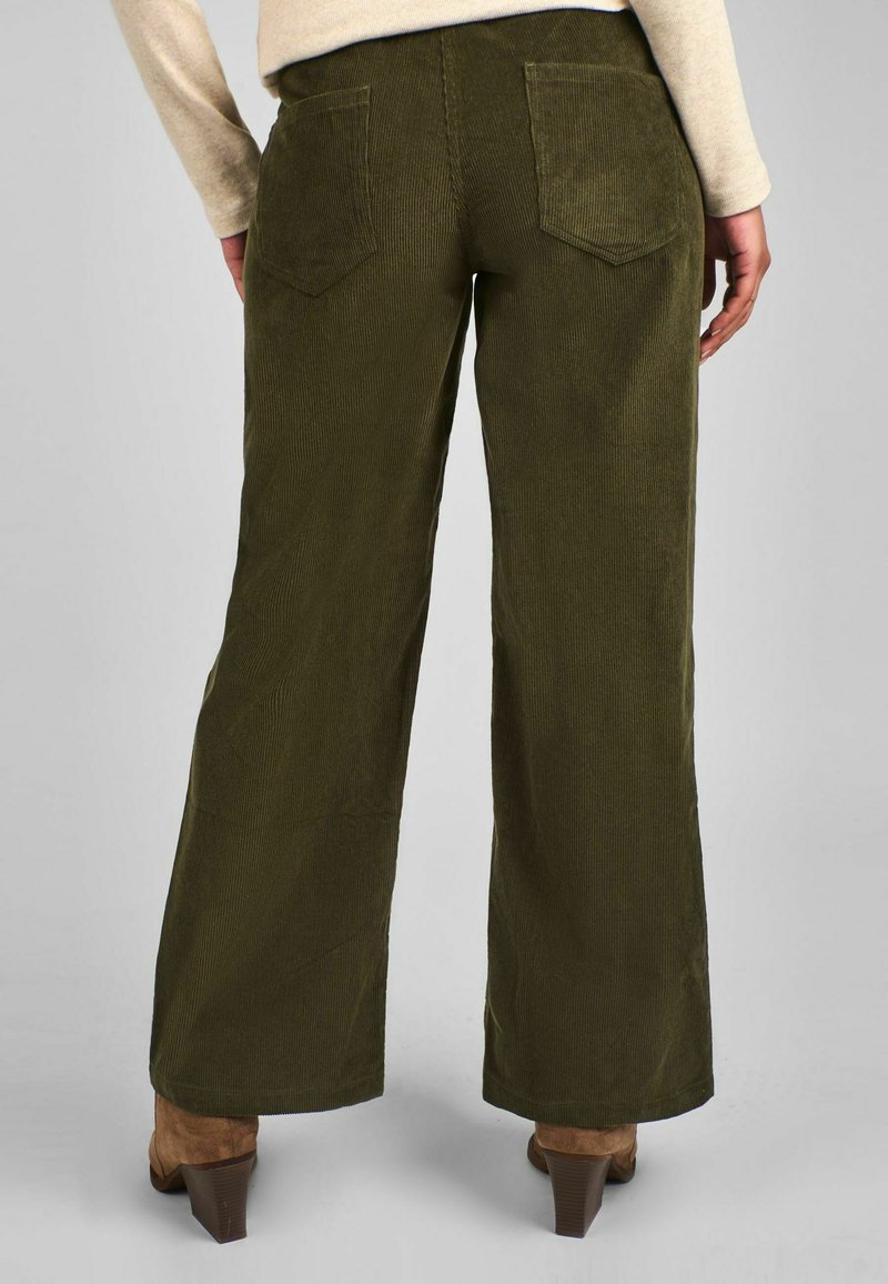 Pantaloni din corduroy verde măsliniu cu un croi larg, având două buzunare pe spate și un finisaj moale texturat. Pantofi maro cu toc mic vizibili.