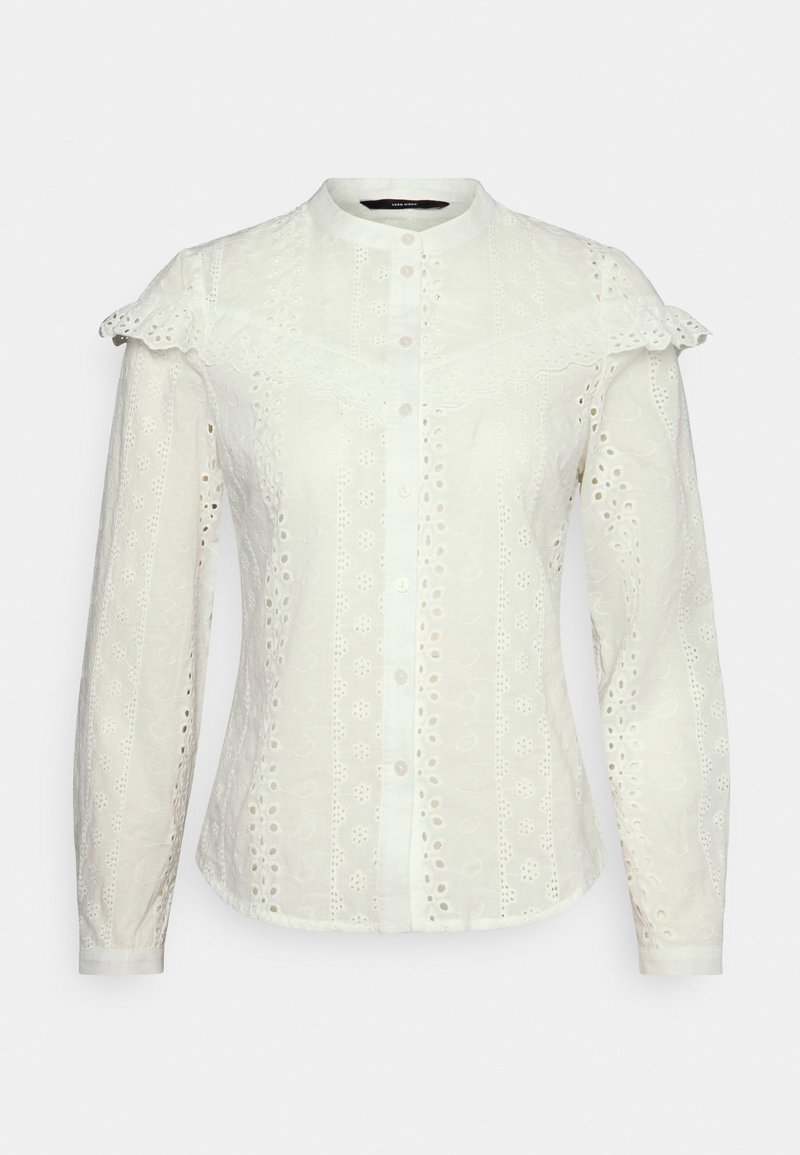 Hvid bluse i struktureret stof, der har lange ærmer, flagrende krave og intrikate broderier med huludskæringer og knapper.