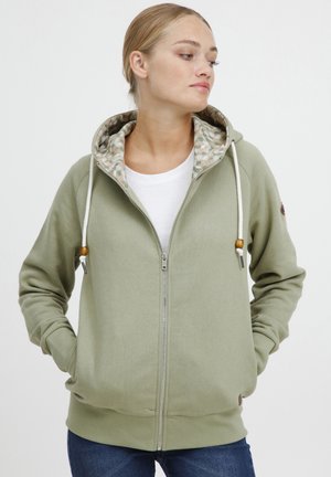 Felpa verde chiaro con zip, dotata di fodera interna a fantasia, cordini regolabili e due tasche laterali. Presenta un orlo e polsini a coste.