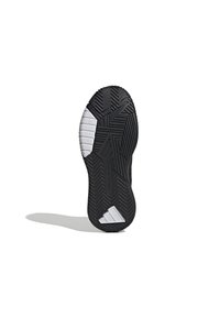 Semelle de chaussure de sport noire avec un caoutchouc texturé, présentant des motifs en zigzag et en chevrons. Accents blancs près du talon et du côté latéral.
