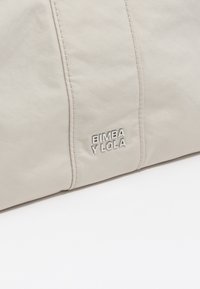 Beżowa torba nylonowa o gładkiej fakturze i subtelnej poświacie, z wytłoczonym logo "BIMBA Y LOLA" w prawym dolnym rogu.