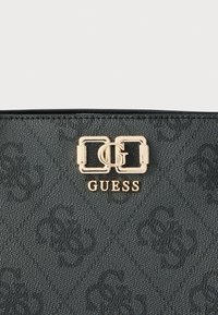 Fekete, texturált kézitáska dombornyomott mintával, aranyszínű dupla G logós csattal és középen elhelyezett "GUESS" márkajelzéssel.