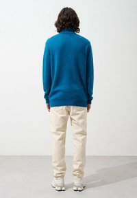 Maglione blu a maglia con colletto alto, abbinato a pantaloni di colore crema. Presenta polsini e orlo a coste, una texture morbida e una vestibilità casual.