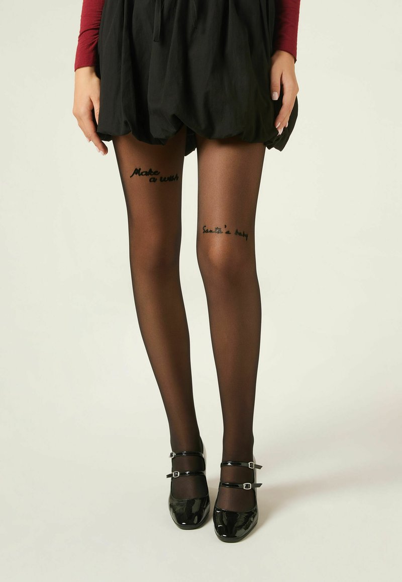 Svart, genomskinlig tights med läsbar text som säger "Önska dig något" och "Jultomtes bebis." Bärs tillsammans med en svart kjol och svarta lackade Mary Jane-skor.