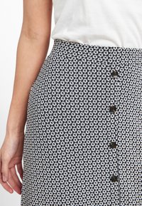 Falda azul marino con un patrón floral blanco, confeccionada con una tela de textura suave. Presenta una fila de botones negros en la parte delantera.