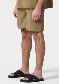 Shorts en kaki en tissu léger, longueur genou avec une taille élastique. Sandales noires à glissière avec des brides croisées et des détails texturés.