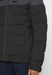 Černá péřová bunda s šedým ramenním kabátem, s horizontálním prošíváním, zapínacími kapsami a elegantním zipovým uzávěrem.