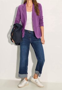 Purple blazer over white top, paired with rolled-up blue denim jeans and white sneakers. The outfit features a casual yet tailored look.