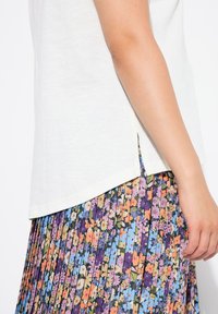 Top blanco de manga corta con abertura lateral, combinado con una falda plisada que presenta un colorido patrón floral en púrpura, azul, naranja y rosa.