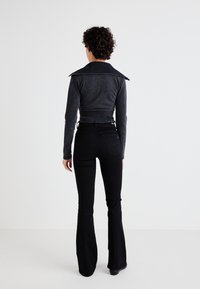 Black flared jeans paired with a fitted, dark gray, corduroy jacket featuring prominent shoulder flaps and a cropped design.