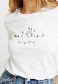 Bílý bavlněný tričko s ilustrací newyorské panorámy z jedné souvislé linie a textem "New York City" pod grafikou.