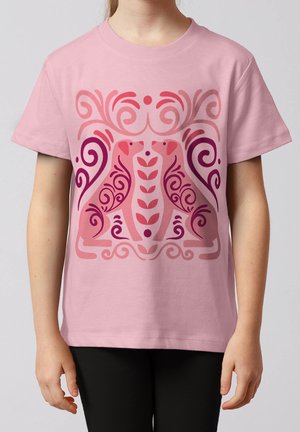 Kind trägt ein rosa T-Shirt mit einem symmetrischen Design von zwei stilisierten Hunden, die sich gegenüberstehen, umgeben von roten und violetten Wirbeln.