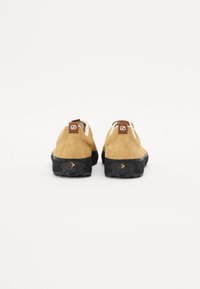 Brown suede climbing shoes with a black rubber sole, featuring a rear pull tab and an orange accent on the heel for functionality.