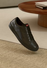 Schwarzer Ledersneaker mit glatter Oberfläche, Schnürdesign und sichtbaren Nähten. Verfügt über ein rotes Logotab an der Ferse und eine Gummisohle.