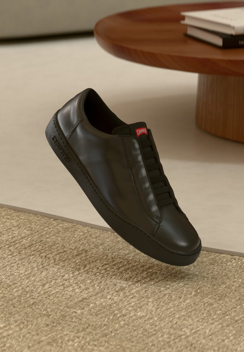 Schwarzer Ledersneaker mit glatter Oberfläche, Schnürdesign und sichtbaren Nähten. Verfügt über ein rotes Logotab an der Ferse und eine Gummisohle.