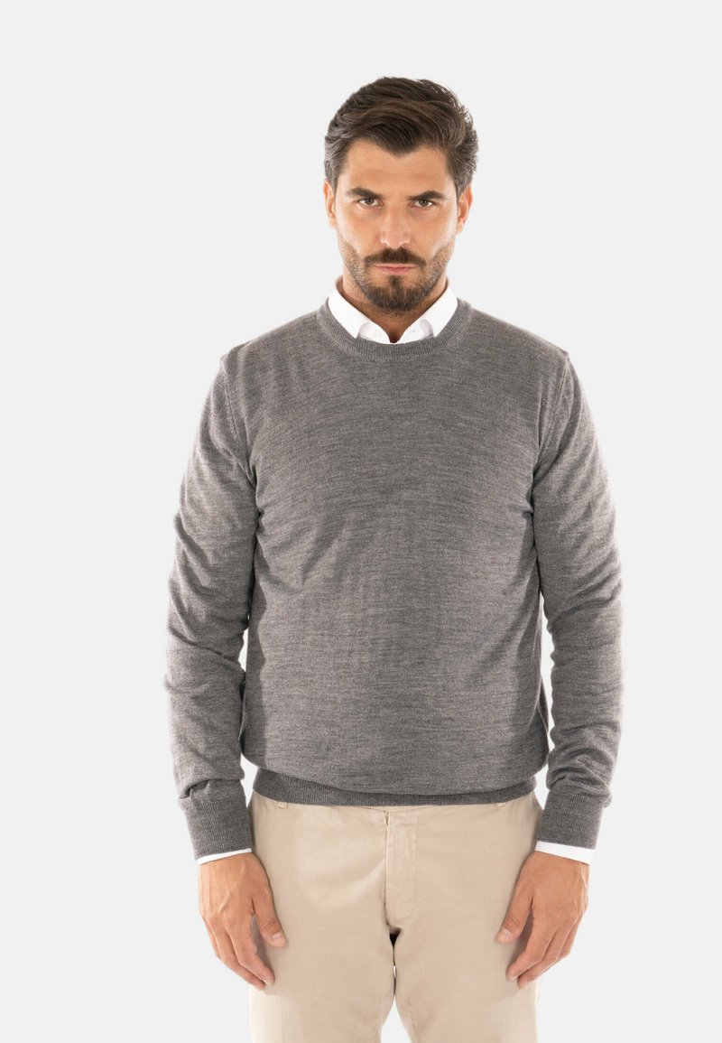 Maglione grigio realizzato in un tessuto morbido, con collo rotondo, maniche lunghe e polsini a costine. Indossato sopra una camicia bianca con colletto.