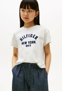 Szary bawełniany t-shirt z napisem "HILFIGER NEW YORK CITY" w kolorze granatowym. Zestawiony z granatowymi spodniami w paski, z guzikami i kieszeniami.