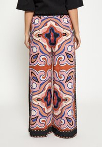 Wijde broek met een kleurrijk abstract patroon in tinten oranje, roze, blauw en zwart, gemaakt van een textuurstof met contrasterende biezen.