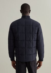 Giacca a vento imbottita blu navy con motivo trapuntato, dotata di collo alto e polsini a costine, realizzata in tessuto morbido e strutturato.