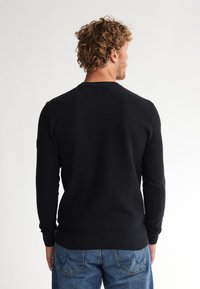 Black knitted sweater with a textured design, long sleeves, and ribbed cuffs. Features a crew neckline and solid color with minimal detailing.