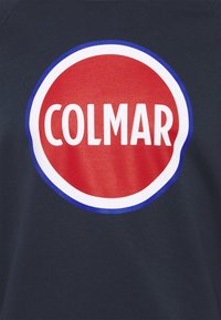 Marinblå sweatshirt med en stor cirkulär röd logotyp där det står "COLMAR" i feta vita bokstäver, omgiven av blå och vita detaljer.