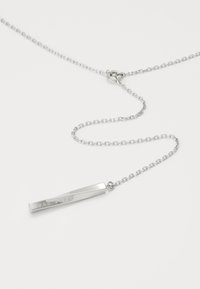 Collier ton argent avec une chaîne fine et un pendentif rectangulaire angulaire gravé "Hugo Boss", présentant une finition métallique polie.