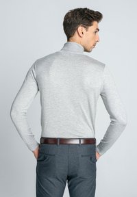 Szary, dopasowany sweter z golfem i długimi rękawami. Gładka tekstura. W połączeniu z ciemnoszarymi spodniami i brązowym skórzanym paskiem. Widok z tyłu.