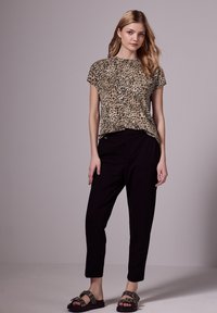Top beige de manga corta con un estampado de leopardo negro, combinado con pantalones negros ajustados y sandalias oscuras con herrajes decorativos.
